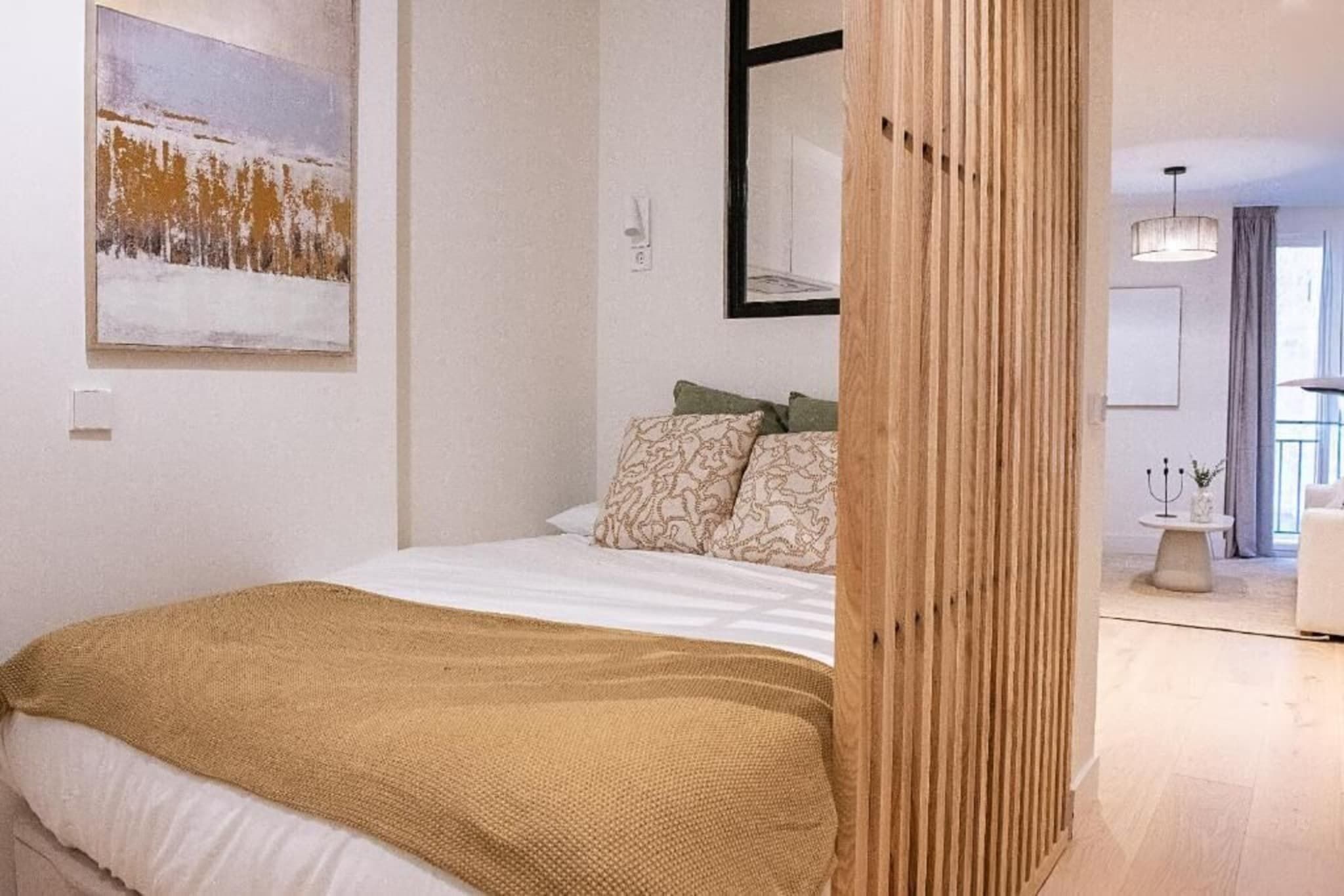 A bedroom with a bed, pillows, a blanket, a painting on the wall, and a wooden partition.