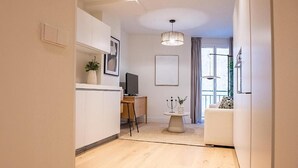 Eine moderne K üche mit weißen Schränken, eine Essecke mit rundem Tisch und ein Wohnzimmer mit einer Couch.