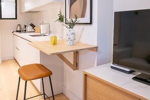 Eine kleine Küche mit einer Holz Arbeitsplatte, einem Hocker, einem Fernseher und einem kleinen Blumentopf.