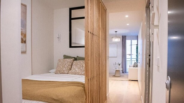 Ein modernes Schlafzimmer mit Bett, einer Holzwand und Blick ins Badezimmer.