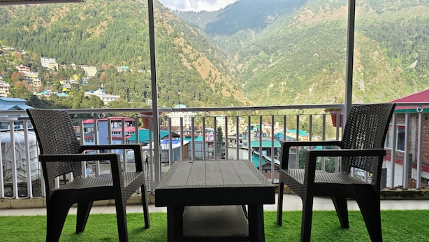 A terrace with a table and chairs, overlooking a mountainous landscape with buildings in the background. - Triund View Homestay (Dharamshala)