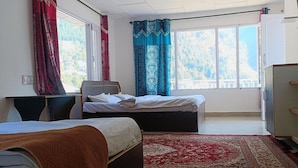 A hotel room with two beds, a desk, a chair, a TV, and large windows with curtains. - Triund View Homestay (Dharamshala)