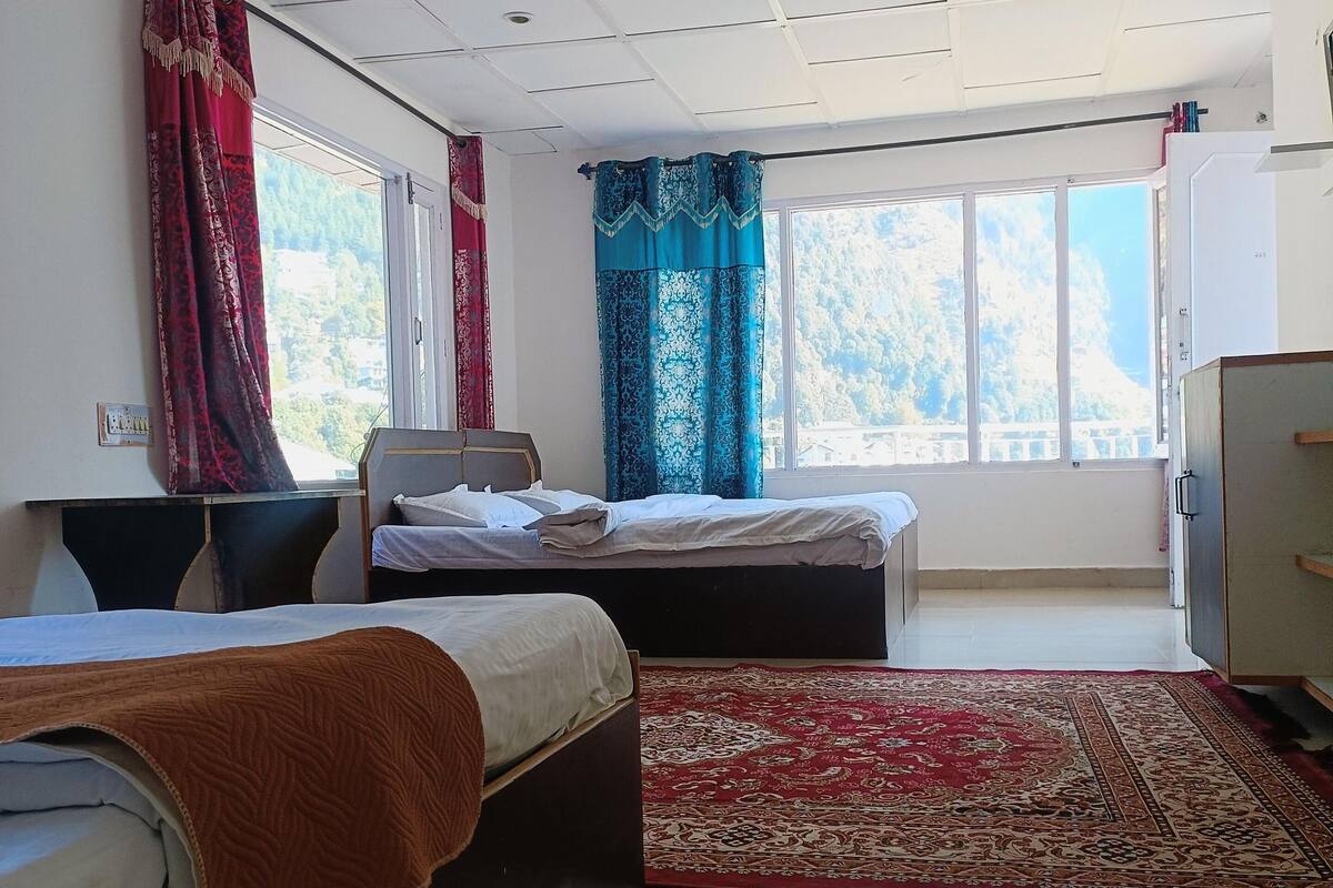 Une chambre d’hôtel avec deux lits, un bureau, une chaise, une télévision et de grandes fenêtres avec des rideaux.