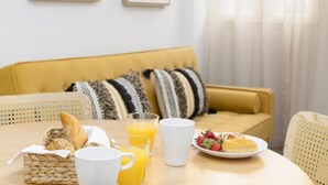 A breakfast setting with a yellow sofa, a woven basket with bread, a plate of strawberries, a glass of orange juice, and a white mug on a wooden table. - TH Peset Aleixandre 5D (Valencia)