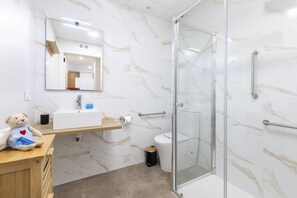 A modern bathroom with a marble backsplash, a glass shower enclosure, and a wooden vanity with a teddy bear. - TH Peset Aleixandre 5D (Valencia)