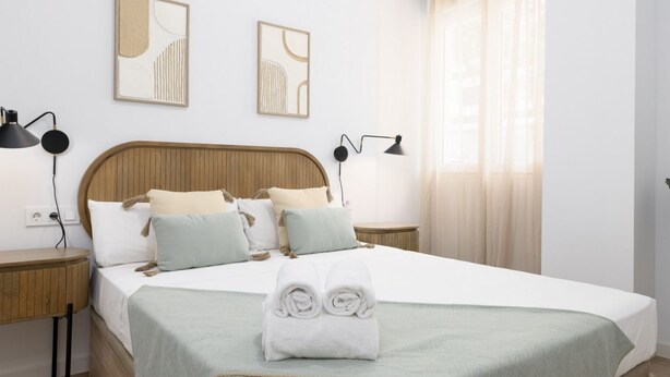A neatly made bed with a green blanket, two bedside tables with lamps, and abstract wall art. - TH Peset Aleixandre 5D (Valencia)