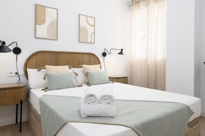 A neatly made bed with a green blanket, two bedside tables with lamps, and abstract wall art. - TH Peset Aleixandre 5D (Valencia)