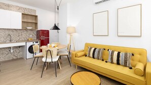 A compact living space with a yellow sofa, a dining table with chairs, a washing machine, and a red refrigerator. - TH Peset Aleixandre 5D (Valencia)