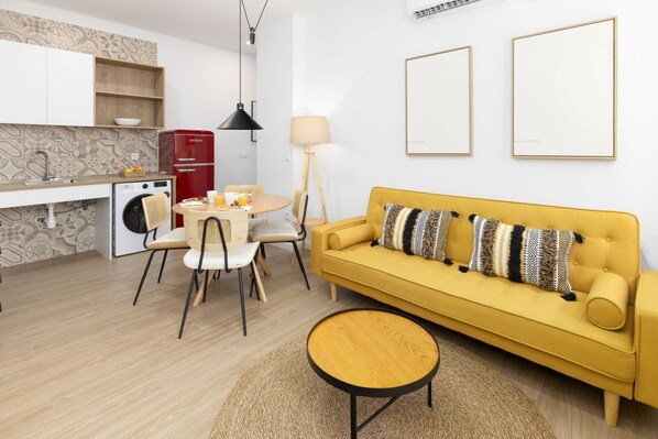 A compact living space with a yellow sofa, a dining table with chairs, a washing machine, and a red refrigerator. - TH Peset Aleixandre 5D (Valencia)