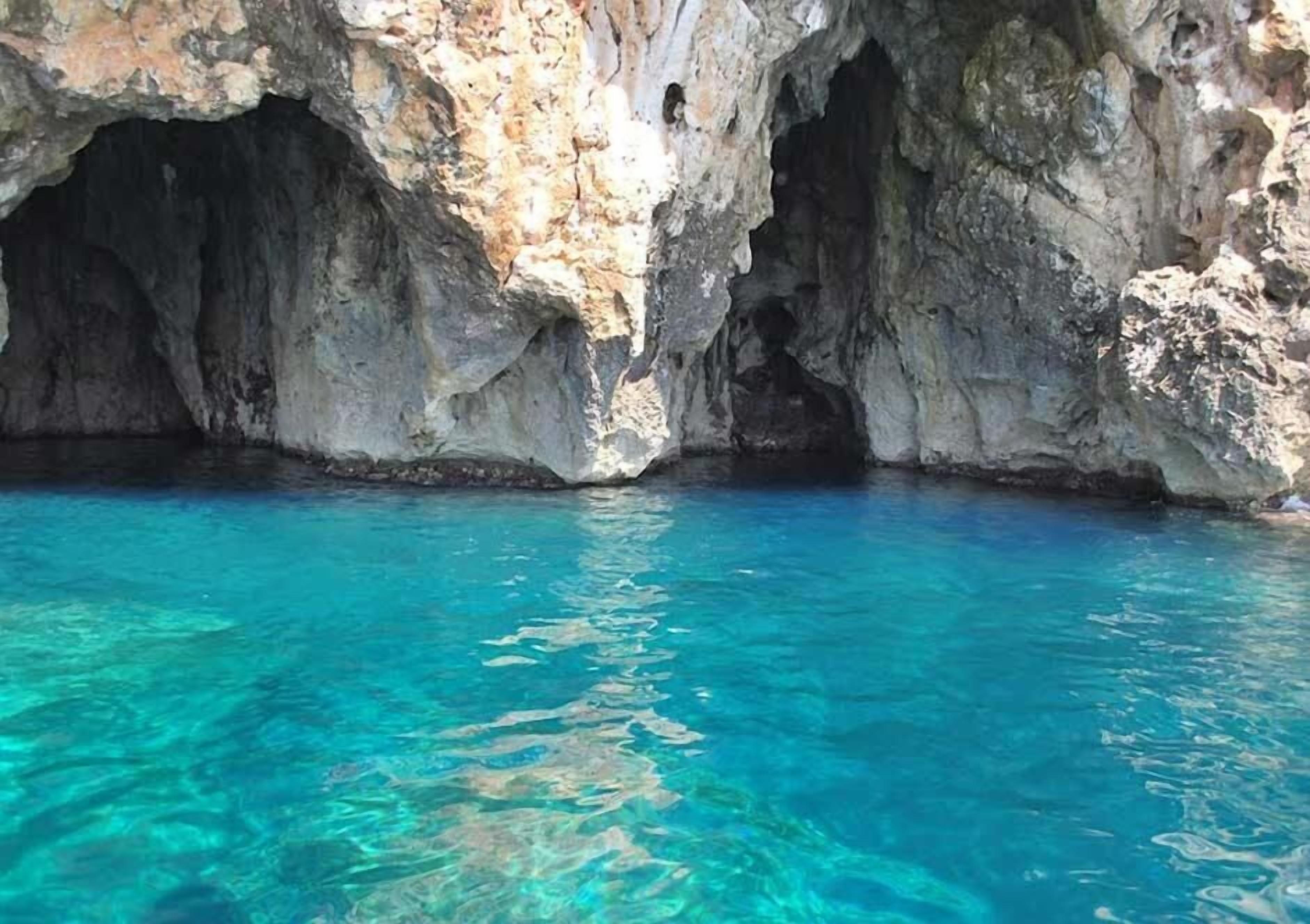 A natural cave with clear blue water at the bottom.