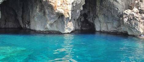 A natural cave with clear blue water at the bottom.
