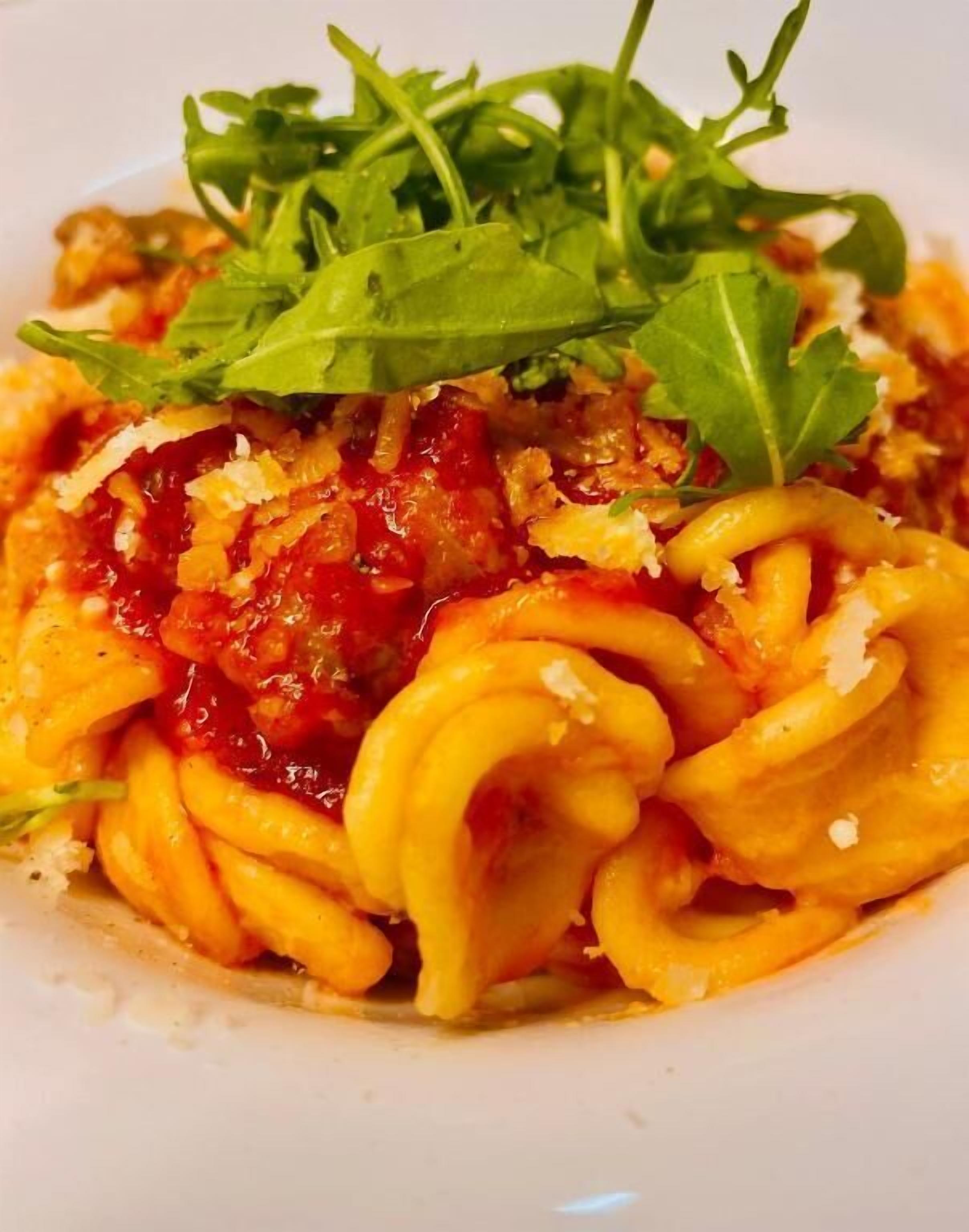 A plate of pasta with a red sauce and a garnish of green leaves.