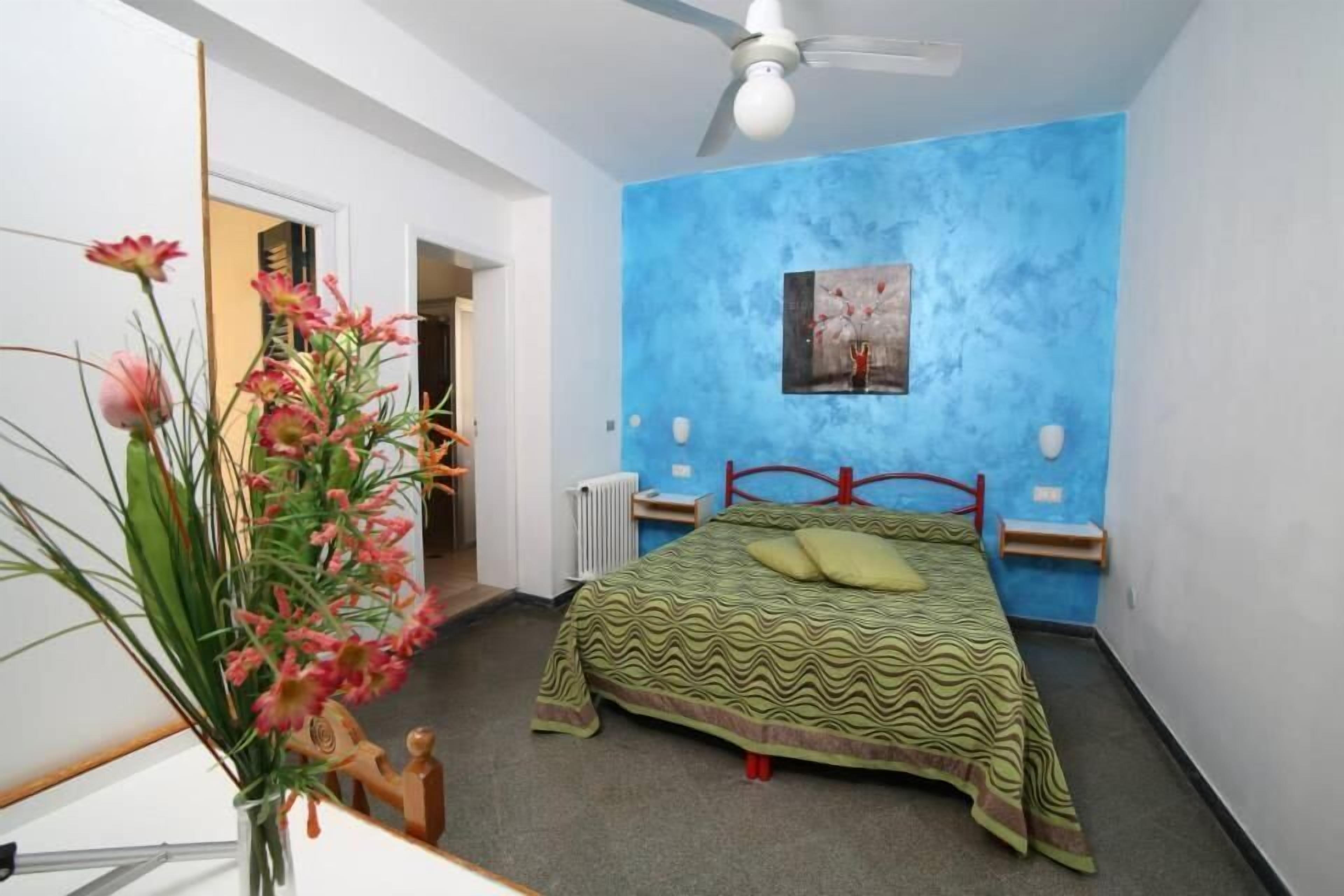 Une chambre à coucher avec un lit, un mur d’accent bleu, un ventilateur de plafond et un radiateur.