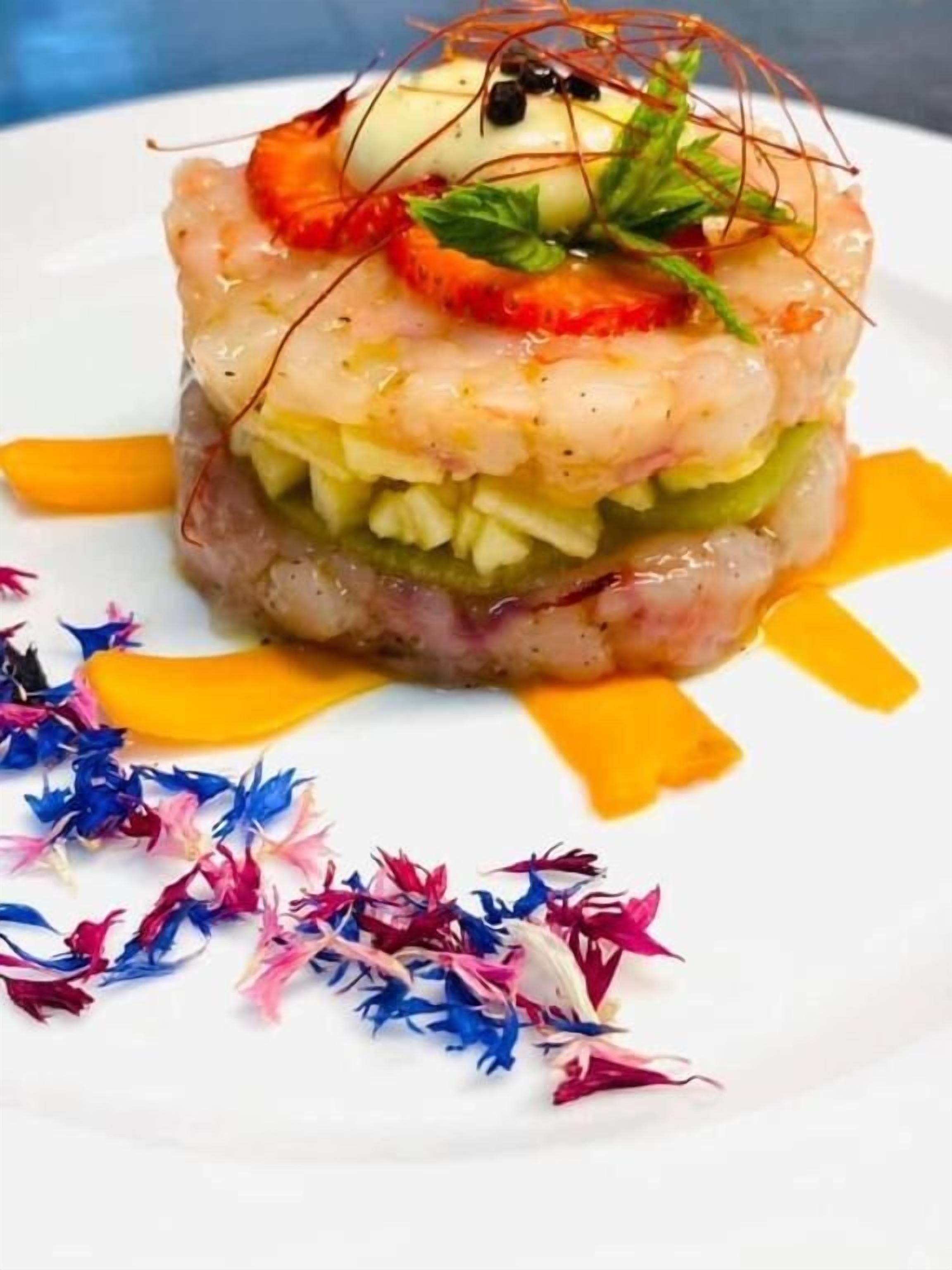 Un plat composé de différentes couches d’ingrédients et agrémenté de garnitures, le tout présenté dans une assiette blanche.