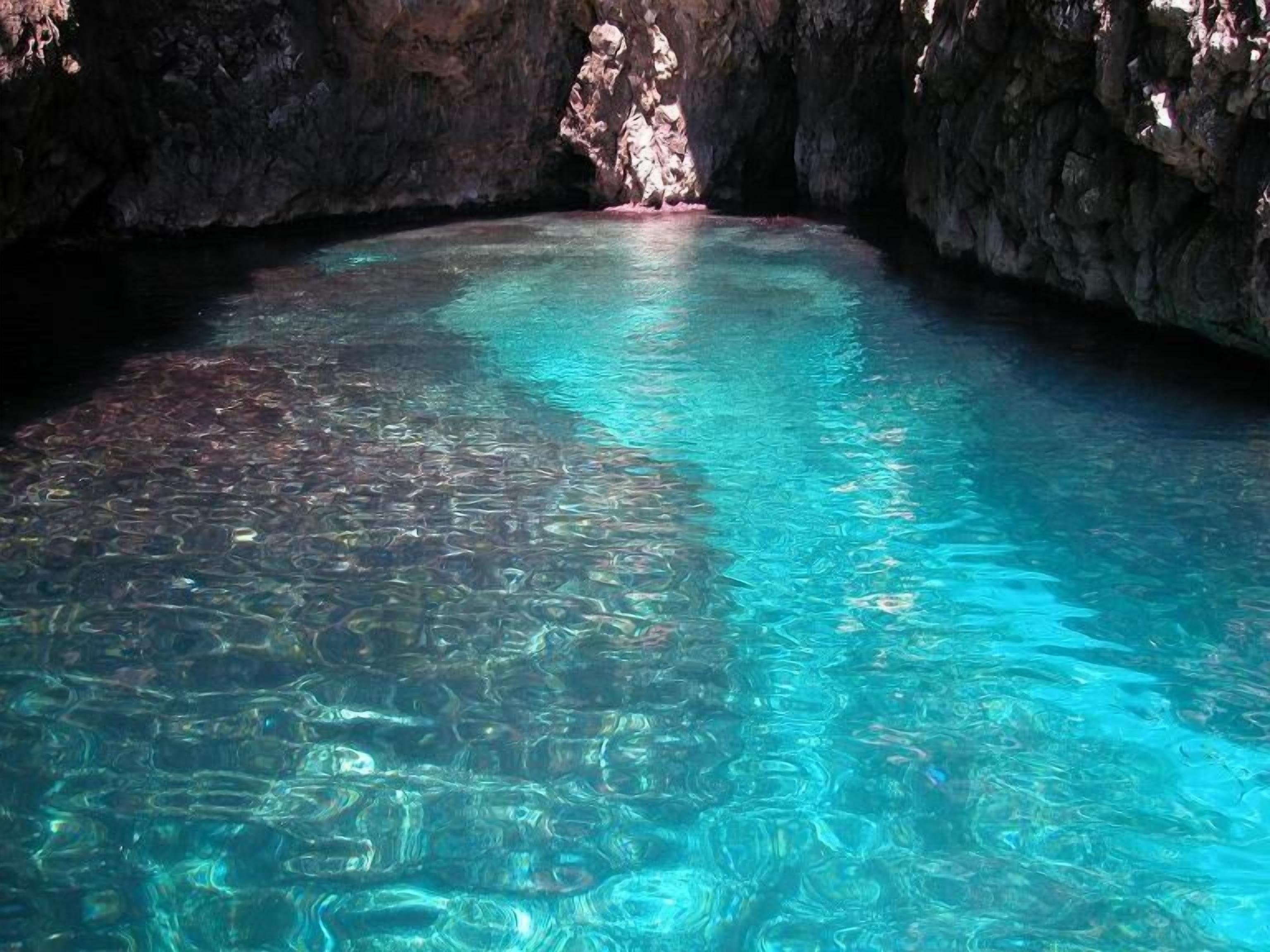 A clear, turquoise pool in a cave with rocky walls.
