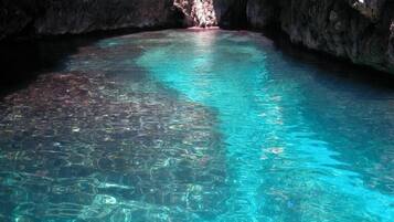 A clear, turquoise pool in a cave with rocky walls.