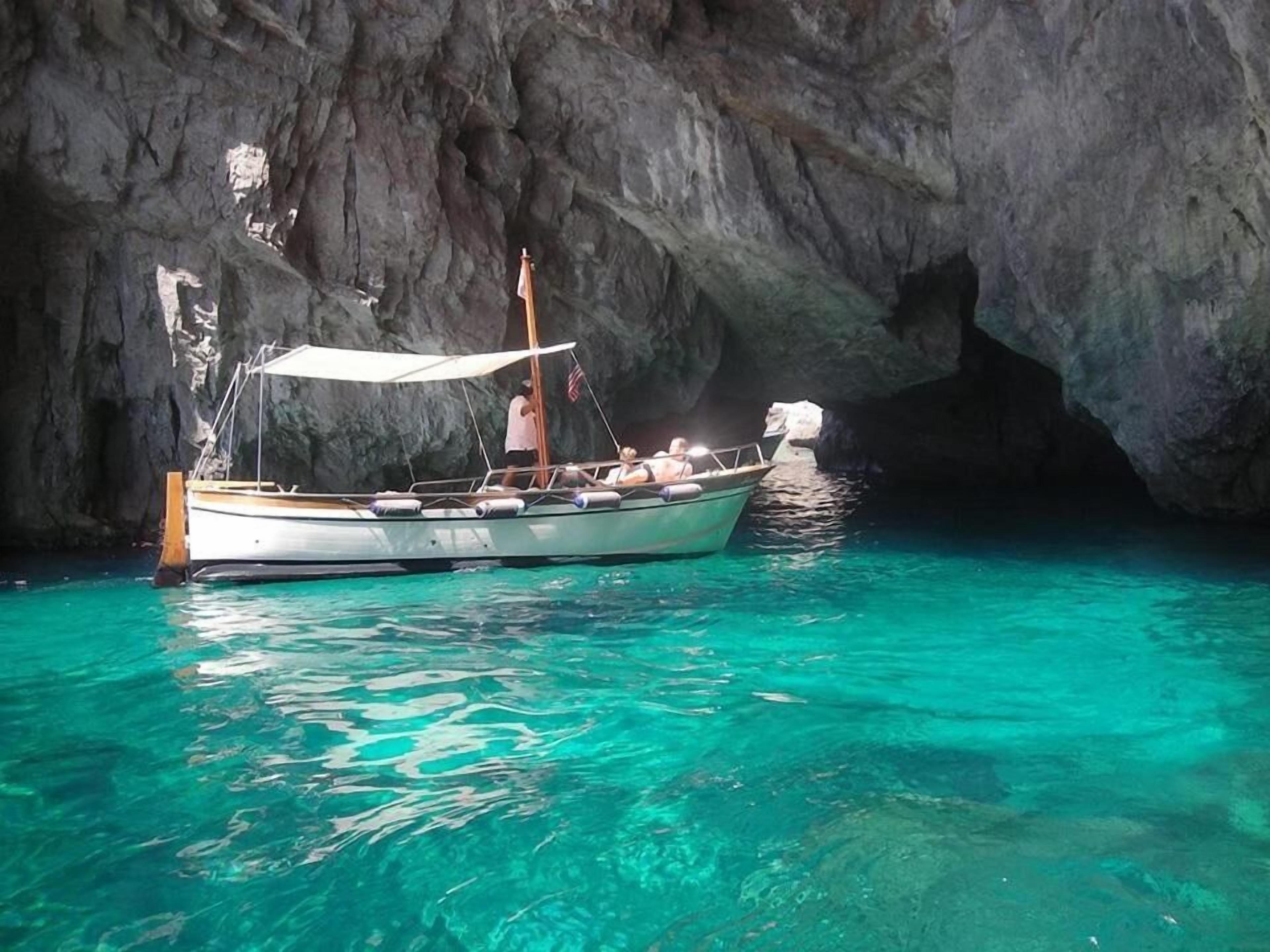 Un bateau était amarré près d’une grotte rocheuse, dans une eau turquoise et cristalline.