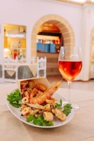 Um prato de mariscos com um copo de vinho tinto sobre uma mesa em um restaurante com decoração clara e portas arqueadas.