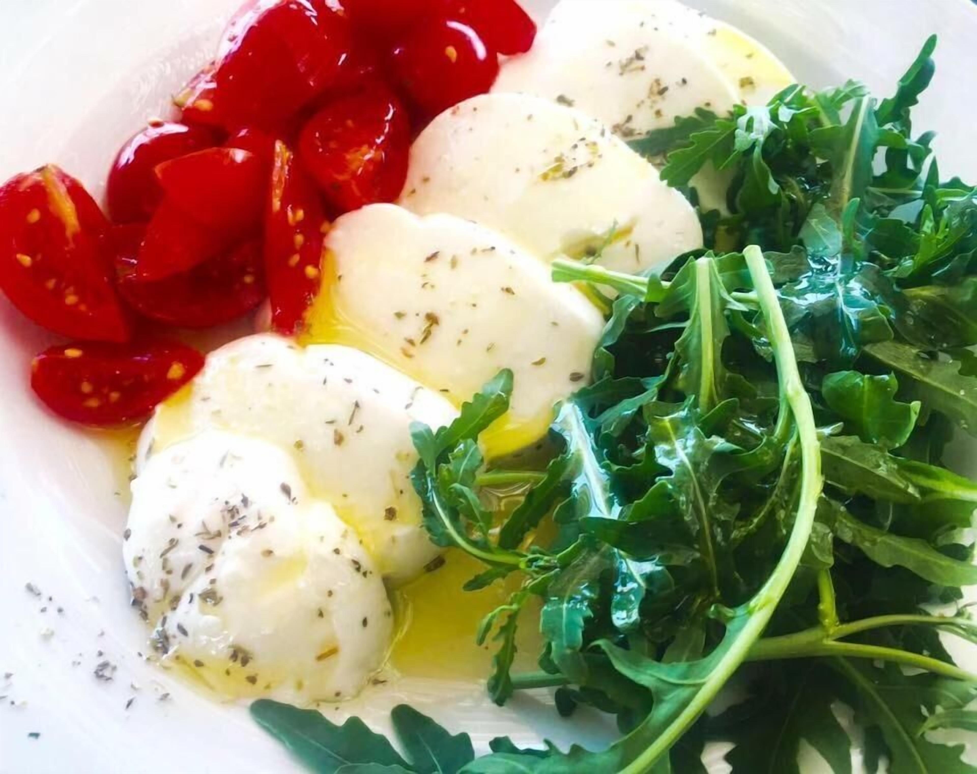 A plate with mozzarella balls, cherry tomatoes, and arugula.