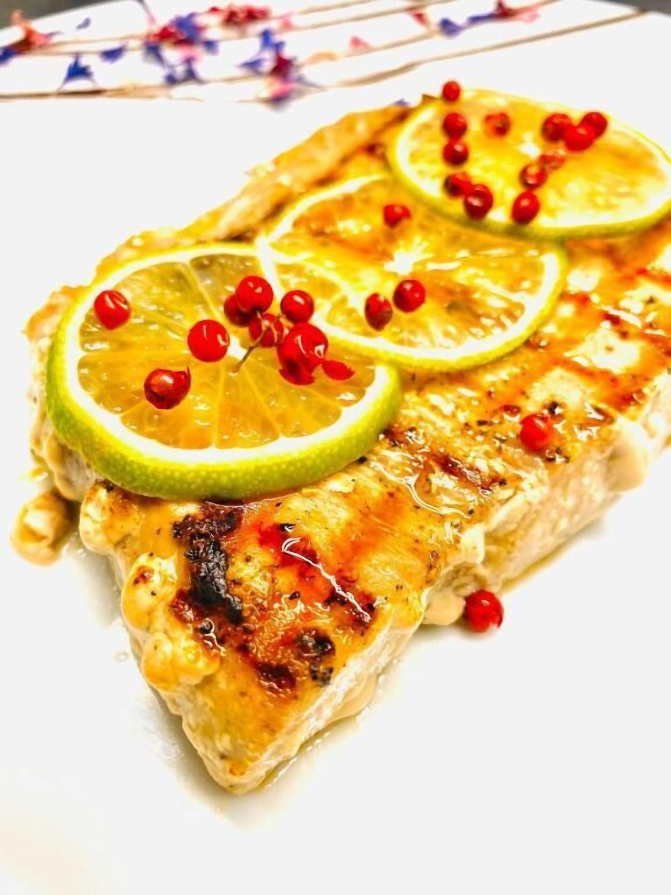 Une assiette de poisson grillé, garnie de tranches de citron et de baies rouges.