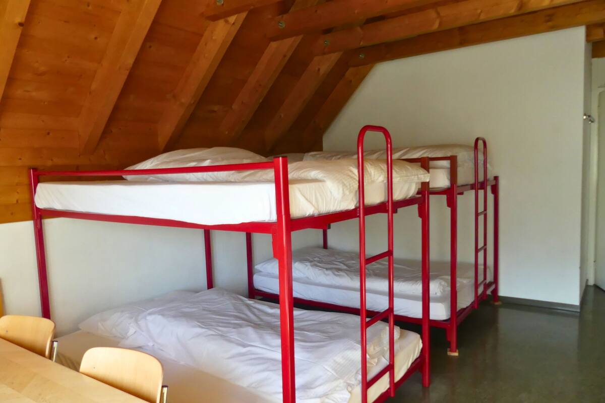 Un dormitorio con literas, vigas de madera en el techo y una mesa sencilla.