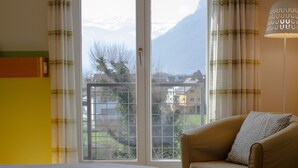 Une chambre à coucher avec un lit, une chaise et une fenêtre donnant sur des maisons et des montagnes.