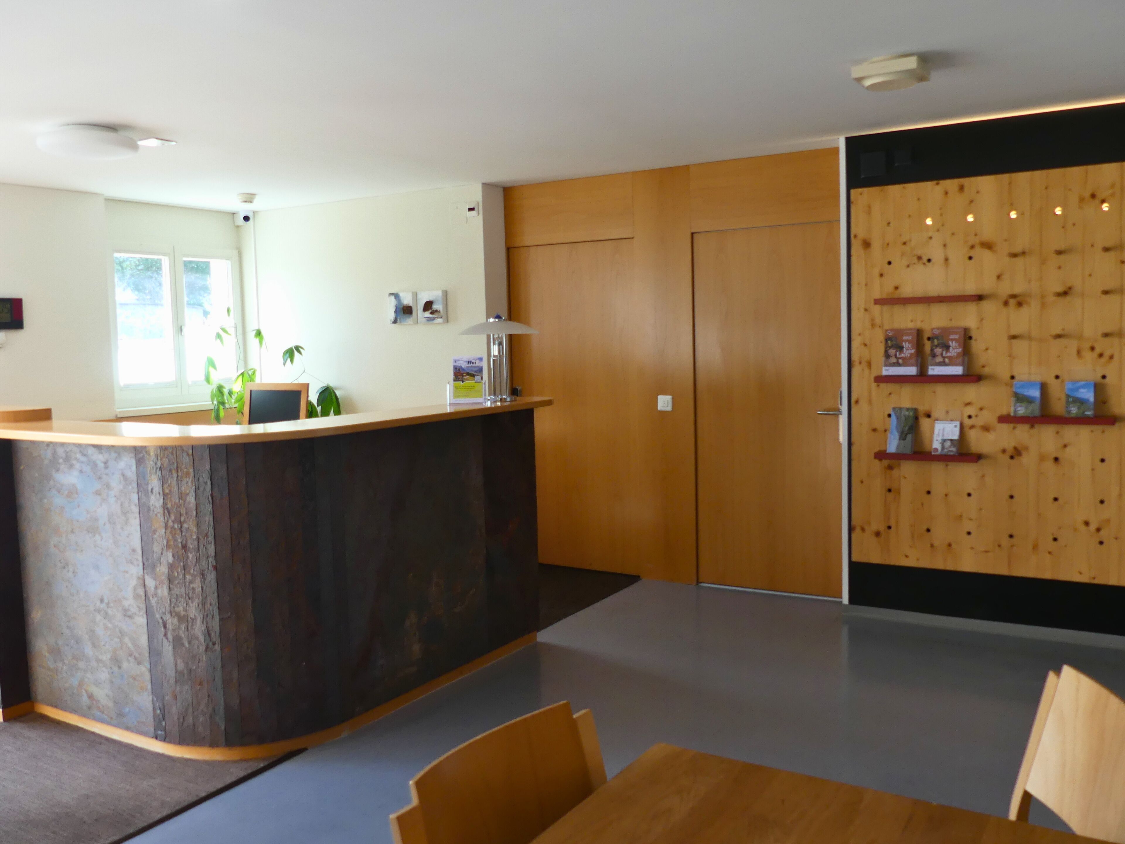 Ein Empfangsbereich mit einem Holzbüro, einer Theke mit einer Lampe, einem an der Wand befestigten Bücherregal und einer Tür mit Holzverkleidung.