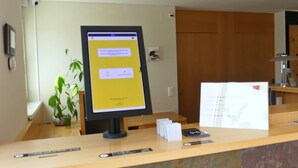 Un comptoir d’accueil avec un écran d’ordinateur affichant un message, une plante et un comptoir en bois.