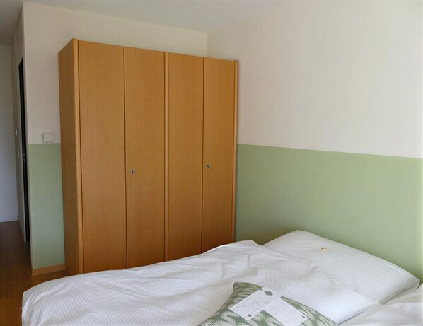 A bedroom with a bed, a wooden wardrobe, and a green and white wall.