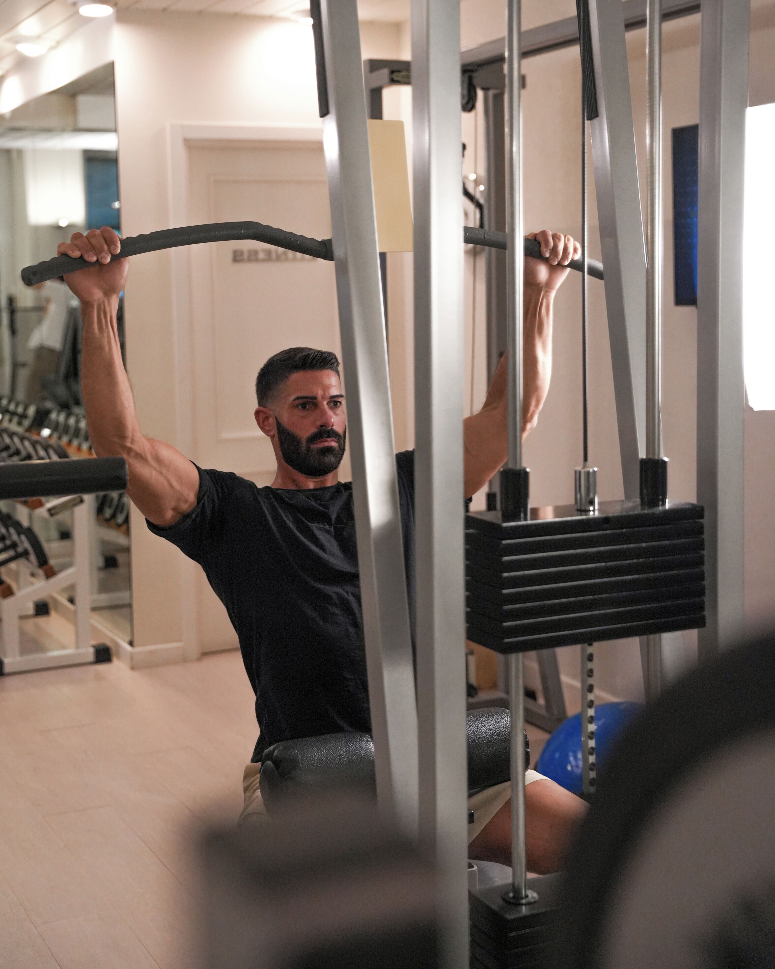 A gym with exercise equipment, a person using a pull-up bar, and a door in the background.