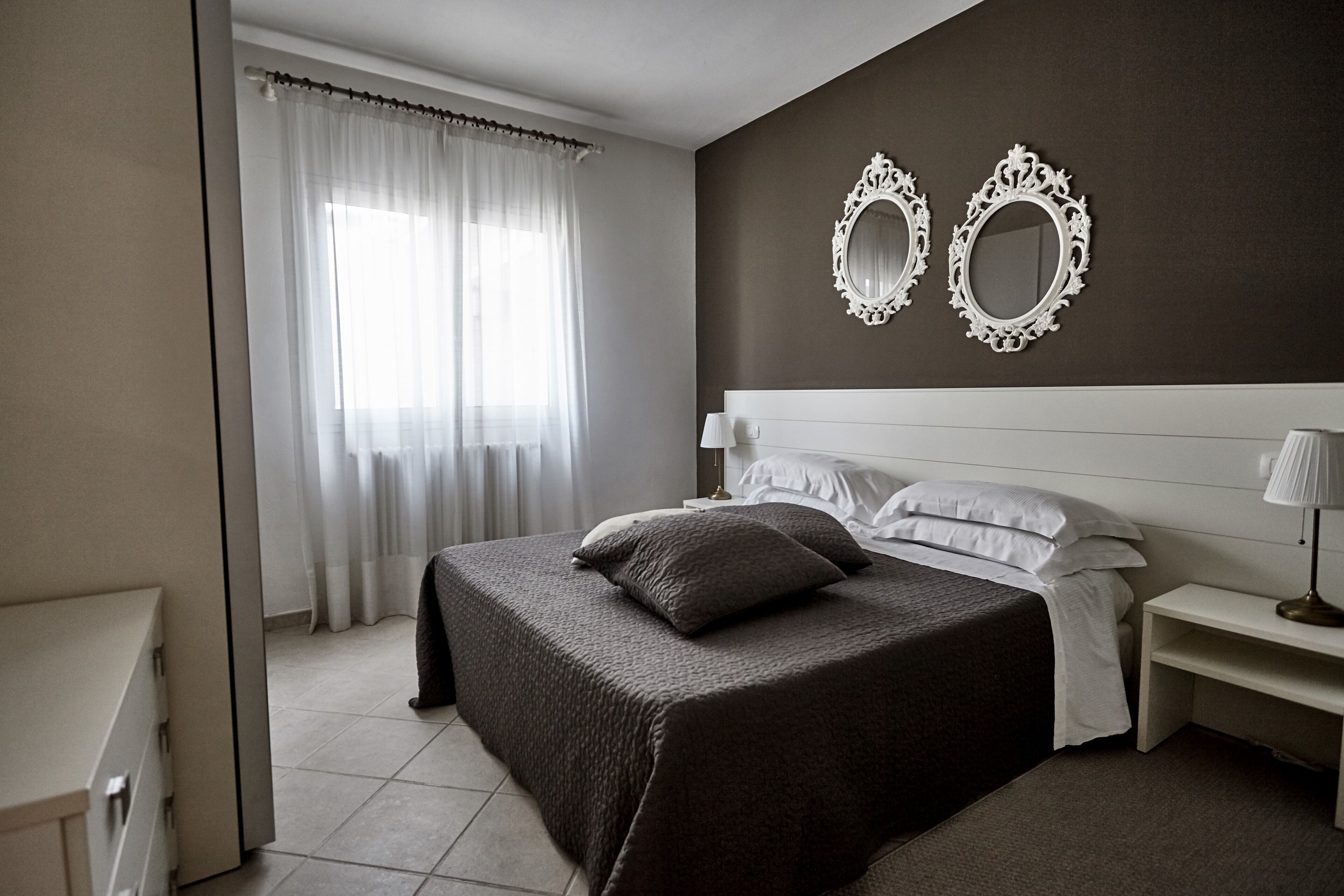 Un dormitorio con cama, mesitas de noche, un espejo y una ventana con cortinas.