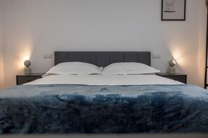 Ein ordentlich bezogenes Bett mit einer blau-weißen Bettdecke, zwei Nachttischlampen und einem gerahmten Zitat an der Wand.