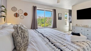 Une chambre à coucher comprenant un lit, un ventilateur de plafond, une fenêtre avec des rideaux, un téléviseur et une commode.