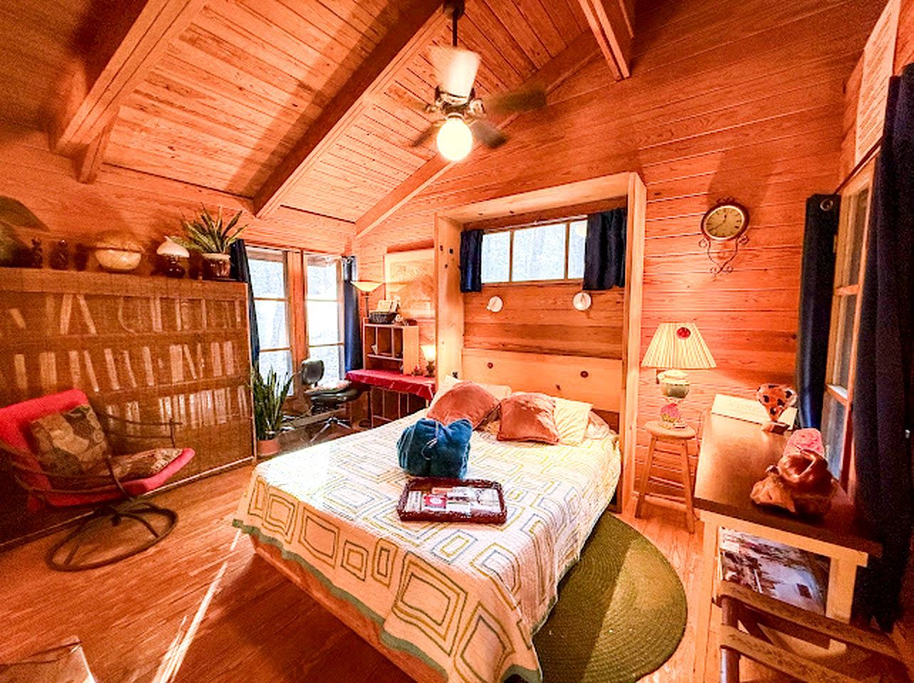 A cozy wooden cabin bedroom with a bed, a chair, a desk, and a window.