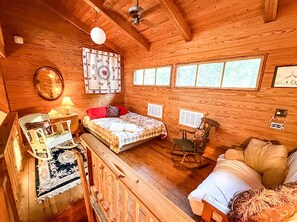 A cozy cabin interior with a bed, rocking chair, and a small table with a lamp.