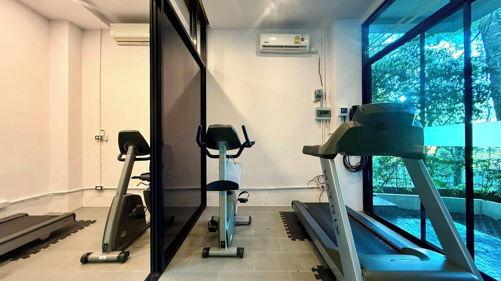 Uma academia com esteiras, bicicleta ergométrica e aparelho de ar condicionado.