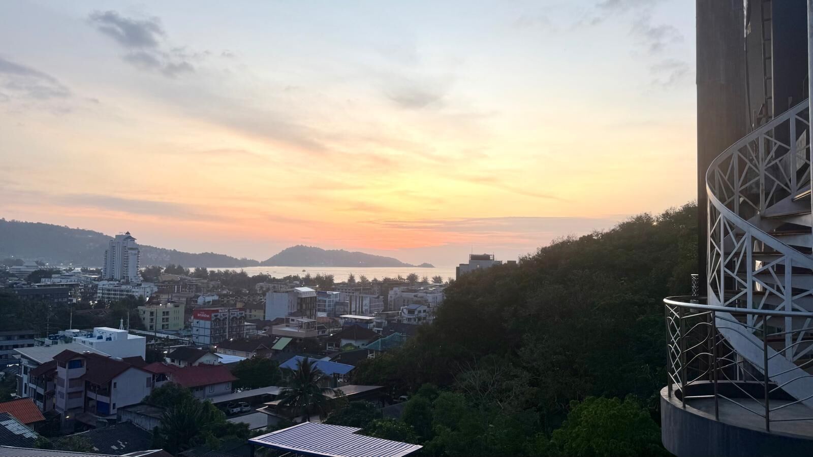 Une vue sur une ville au coucher du soleil, avec des bâtiments et une colline en arrière-plan.