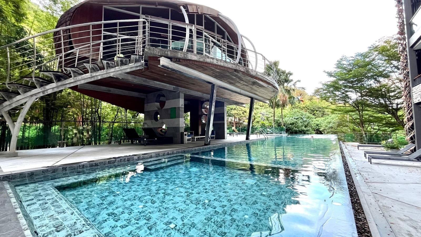 Une piscine avec une terrasse en bois et un bâtiment circulaire doté d’un balcon.