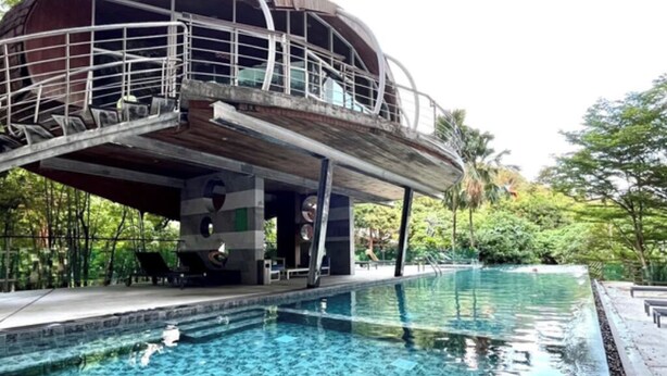 A swimming pool with a unique architectural structure above it, surrounded by lush greenery. - Emerald Terrace Patong (Patong)