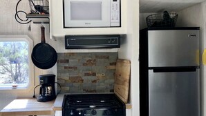 Uma cozinha compacta com fogão a gás, micro-ondas, geladeira e cafeteira.