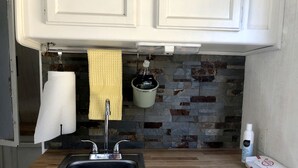 Uma cozinha com bancada de madeira, pia de aço inoxidável, suporte para panelas pendurado e porta-toalhas.