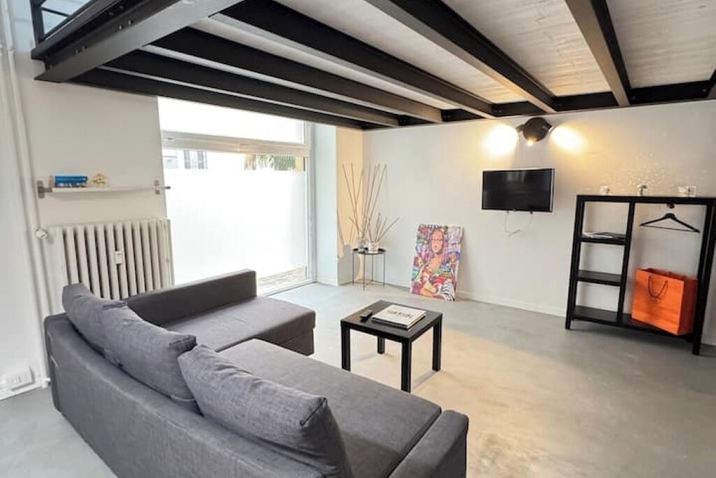 Een moderne woonkamer met een grijze bank, een klein tafeltje, een aan de muur bevestigde televisie en een radiator.