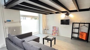 A modern living room with a grey sofa, a small table, a TV mounted on the wall, and a radiator.