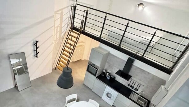 A modern kitchen with a central island, a dining area with a round table, and a staircase leading to an upper level.