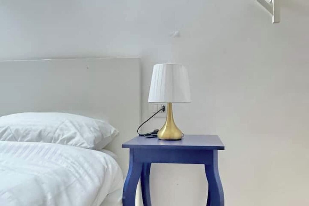 A bed with white linens and a blue bedside table with a lamp.