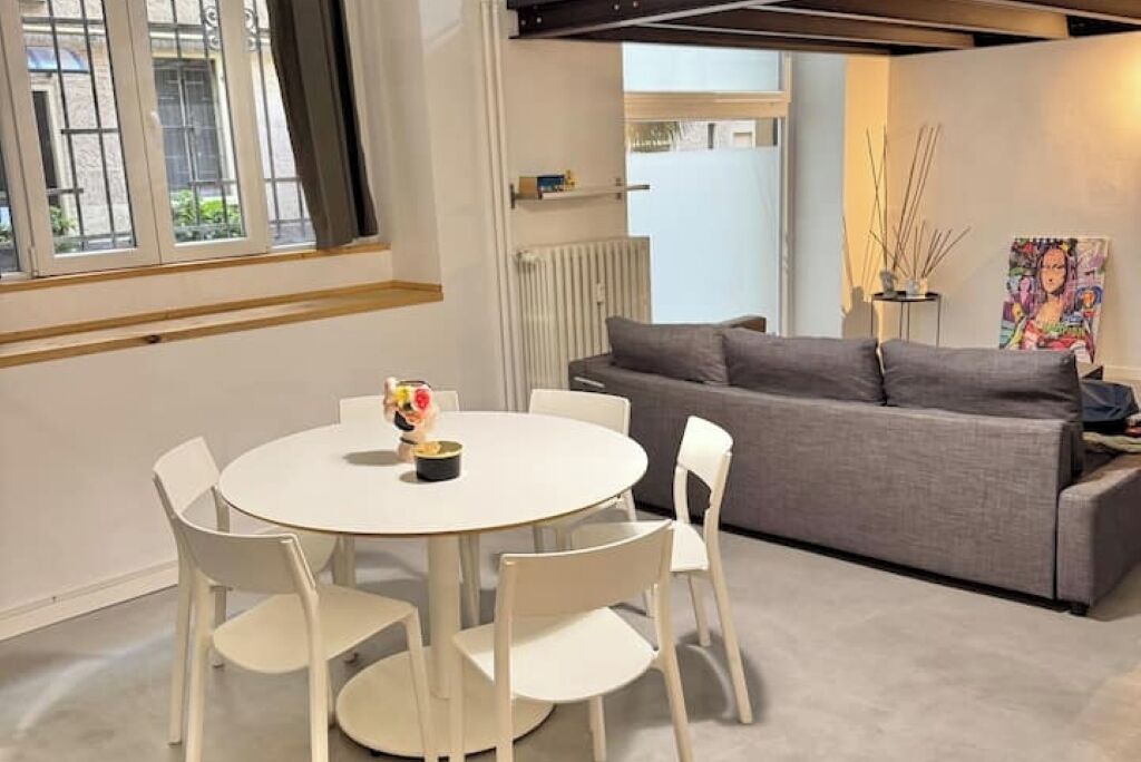 Een moderne woonkamer met een ronde witte tafel, vier witte stoelen, een grijze bank en een radiator.