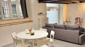 A modern living room with a round white table, four white chairs, a grey sofa, and a radiator.