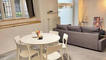 Een moderne woonkamer met een ronde witte tafel, vier witte stoelen, een grijze bank en een radiator.