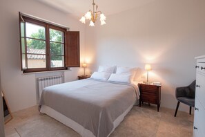 A bedroom with a bed, two bedside tables with lamps, a chair, a dresser, and a window with a view of trees.