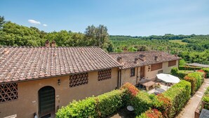 Una villa tradizionale con tetto in tegole, un patio con mobili da esterno e vista sulla campagna circostante.